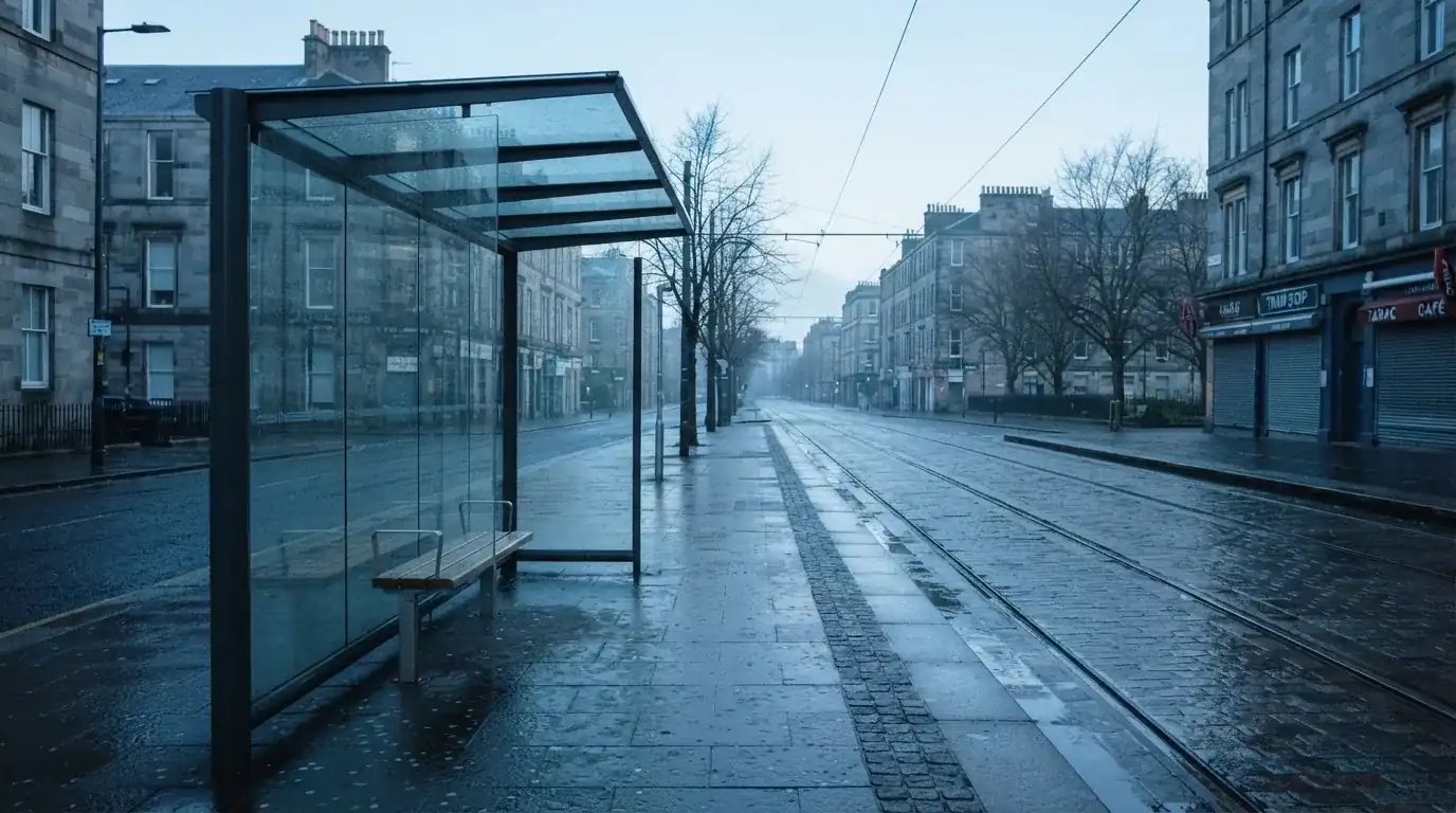 Pusta wiata przystanku tramwajowego na miejskiej ulicy o świcie, pusta ławka i mokry chodnik.