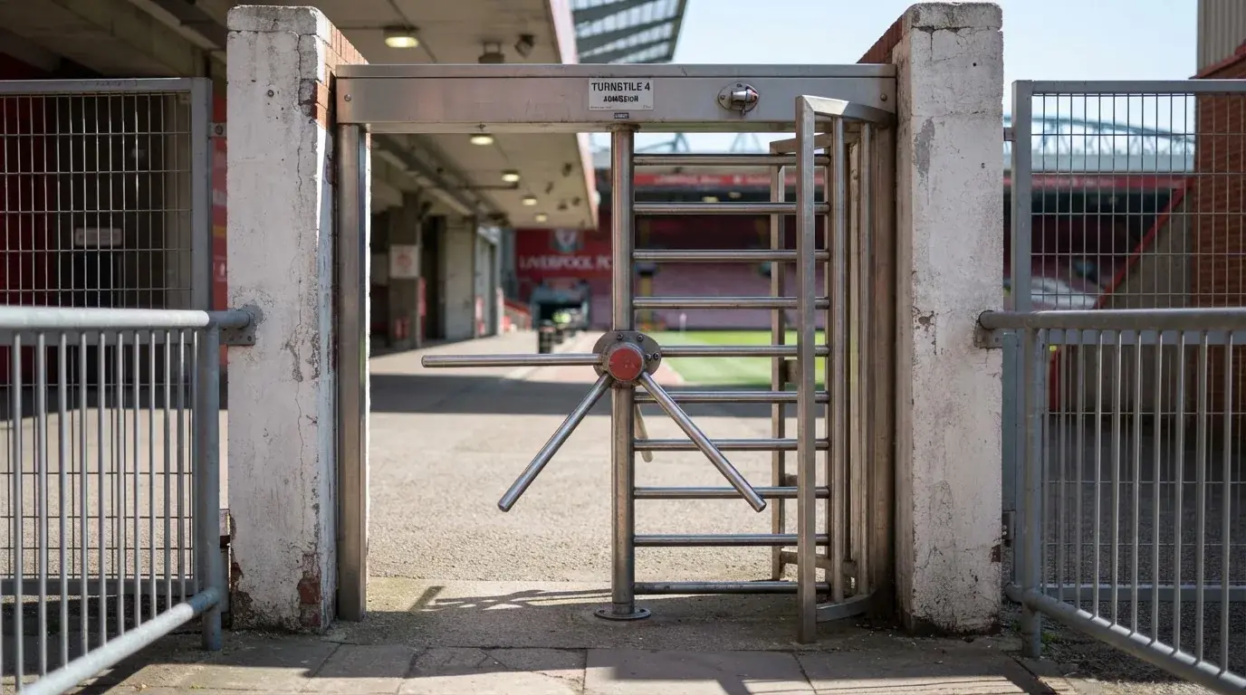 Metalowa bramka obrotowa przy pustym wejściu na stadion w świetle dziennym, pręty łapią blask słońca.