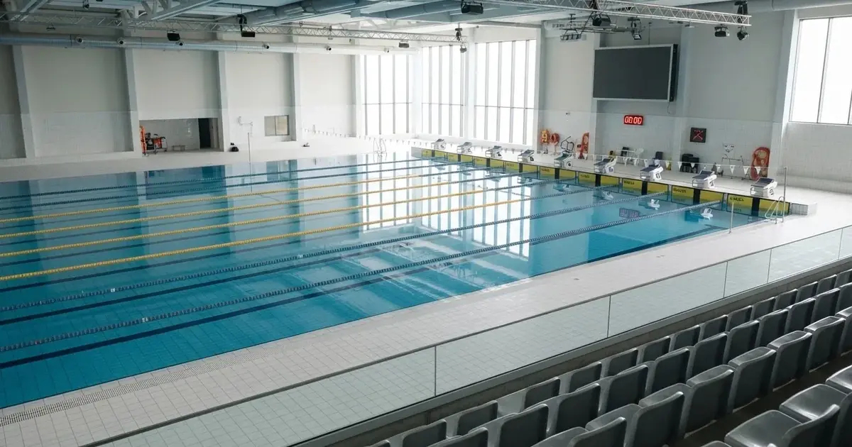 Pusty basen olimpijski z równymi torami i spokojną taflą wody, widok z trybun w jasnym świetle.